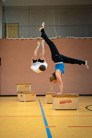 Impressionen von den letzten Veranstaltungen. In dem Bild: eine Person, die einen Handstand auf einem Kasten macht. Im Hintergrund ist eine weitere Person, sie einen Salto über eienen Kasten macht.